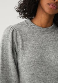 Grå strikket sweater med rund halsudskæring og subtil puffet ærmedesign. Blød tekstur og ensartet farve.