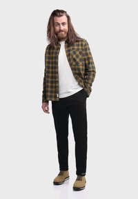 Grünes und gelbes Karomusterhemd, weißes T-Shirt, schwarze Hose und braune Stiefel. Das Hemd hat Knöpfe und eine Brusttasche; das Modell steht frontal.