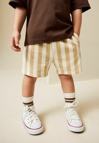 Hellfarbene gestreifte Shorts in Beige und Creme, kombiniert mit weißen Turnschuhen und braun akzentuierten Socken, mit lockerem Schnitt und Taschen.