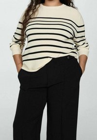 Pull rayé crème avec des lignes horizontales bleu marine, avec un col rond et des poignets côtelés, associé à un pantalon large noir avec poches.