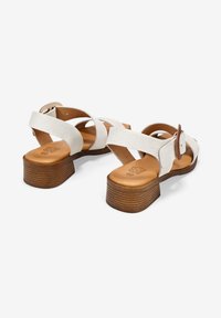 Sandalias de cuero blancas con correas cruzadas, punta redonda y tacón de bloque de madera marrón. Incluyen una correa de tobillo ajustable y material texturizado.