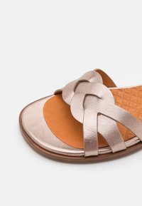 Sandal de color oro rosa metálico con un diseño superior trenzado, plantilla texturizada marrón y suela curva suave.