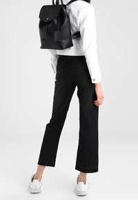 Czarny skórzany plecak z zaokrągloną klapką, zamknięciem na sznurek i prostokątną metką. Połączony z czarnymi jeansami z wysokim stanem i białymi trampkami.