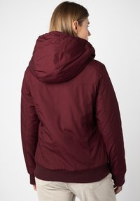 Burgundy hooded jacket with a fitted design, elastic cuffs, and a textured fabric. The back showcases a smooth finish and minimal detailing.