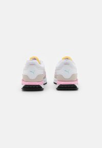 Sneaker Puma con tomaia in mesh e suede bianco, dettagli in rosa e beige, tallone imbottito e suola in gomma nera. Rivestimento interno giallo.