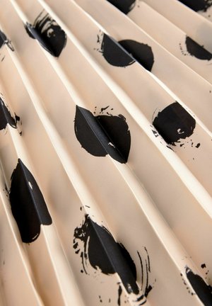 Záhybová textília s béžovým pozadím a výraznými čiernymi kruhovými vzormi. Textúra je hladká, čím vytvára dynamický vizuálny efekt.