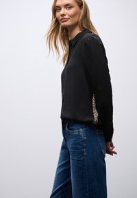Sort knappet skjorte med et slankt design; har leopardprint detaljer på siden. Sættes sammen med blå denim jeans.