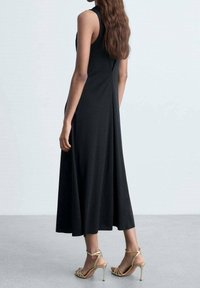 Robe noire sans manches avec une silhouette fluide en A. Accompagnée de talons dorés à lanières. Tissu lisse avec un design minimaliste.