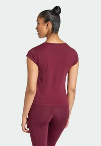 Donkerrode top met korte mouwen en een zachte textuur. Voorzien van een klassieke ronde hals en een licht aansluitend model, gezien van achteren met bijpassende leggings.