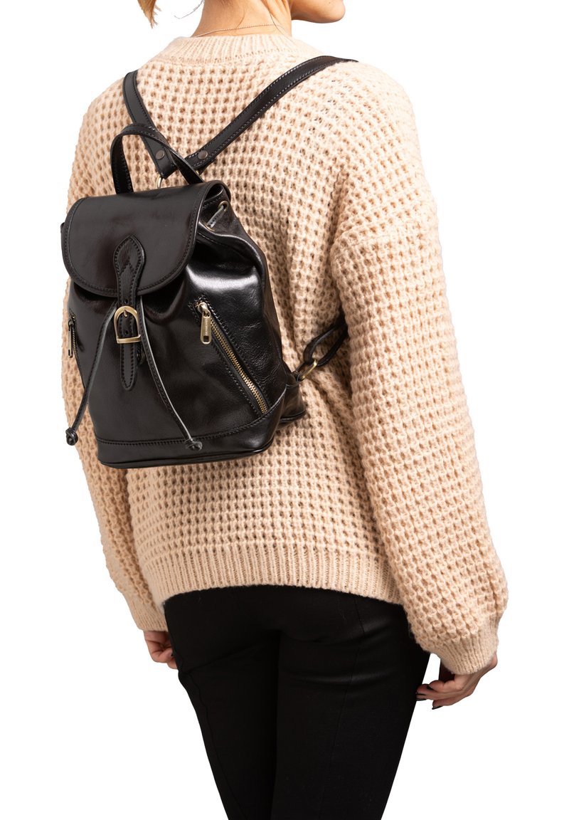 Sac à dos en cuir noir avec un rabat à l'avant, des bretelles ajustables et deux poches zippées. Porté sur un pull en tricot beige.