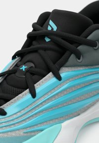 Close-up de um sapato de corrida preto e turquesa com atacadores pretos e painéis laterais texturizados em azul e cinza.