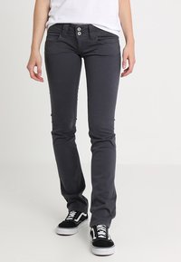 Grå slim-fit jeans med två knappar, framfickor och slitningar, i kombination med svarta och vita sneakers.