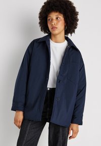 Camicia overshirt blu navy realizzata in tessuto leggero, con colletto a punta, bottoni frontali, taschino sul petto e maniche lunghe.