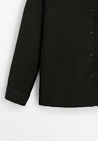 Chemise noire à boutons avec manches longues, en tissu texturé, présentant des poignets arrondis et six boutons assortis sur le devant.