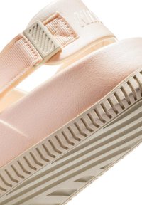 Sandal de goma rosa con una correa texturizada, que presenta una hebilla acolchada y una suela acanalada beige para tracción y comodidad.