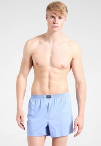 Šviesiai mėlyni medvilniniai šortai su elastine juosmens juosta, turintys priekyje užsegimą ir lygų paviršių. Be papildomų raštų ar akcentų.