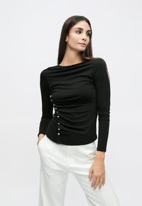 Μαύρο μακρυμάνικο τοπ με ραφές που δημιουργούν πιέτες και ασημένια κουμπιά στη μία πλευρά. Μαλακό, ελαστικό ύφασμα, εφαρμοστό σχέδιο και στρογγυλή λαιμόκοψη.