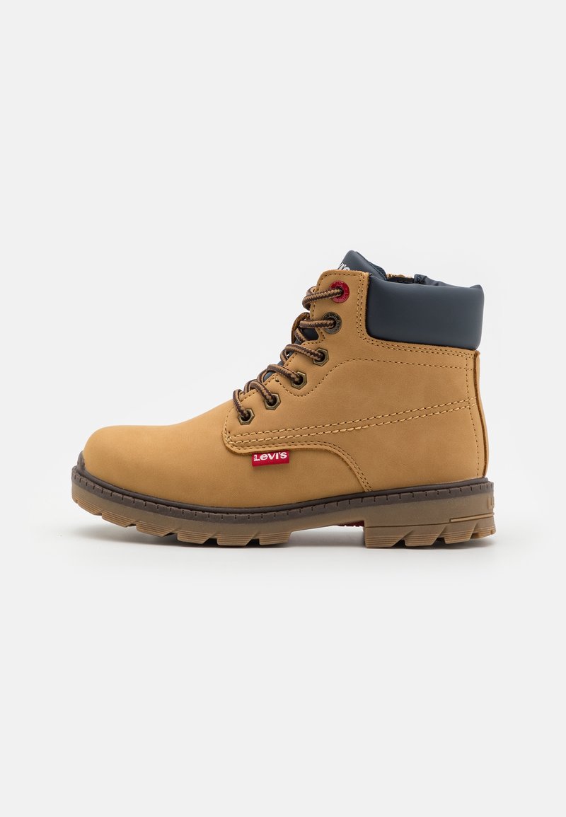 Bottine en cuir couleur tabac avec col noir matelassé, lacets marron, semelle robuste et étiquette rouge avec le logo Levi's sur le côté.
