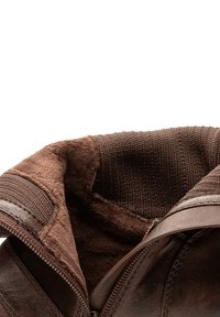 Primer plano de una bota de cuero marrón que muestra el suave forro de fieltro y el puño de tejido de punto con la cremallera parcialmente desabrochada.