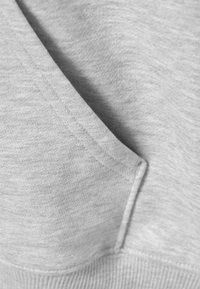 Nærbilde av grå hettegenserstoff, med en teksturert overflate, synlige sømmer og detalj fra en lomme. Mykt materiale.