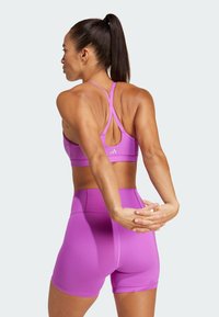 Sujeción deportiva morado con tirantes entrecruzados y pantalones cortos de talle alto a juego. Tela suave y elástica con costuras m�ínimas y detalle de logo.