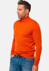 Helle orange Rollkragenpullover, taillierte Passform, gerippte Bündchen und Saum, weicher Stoff, kombiniert mit blauen Jeans und einem geflochtenen braunen Gürtel.
