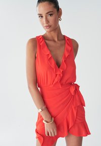 Rode rimpeldress met een diepe V-hals, een cinched taille en een zijstrikdetail. Gemaakt van een lichte stof, met een gelaagde zoom en een gladde textuur.