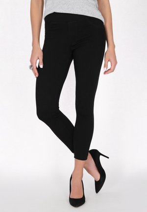 Sorte leggings med en glat tekstur og tætsiddende design, parret med sorte højhælede sko. Elastiklivet giver komfort.