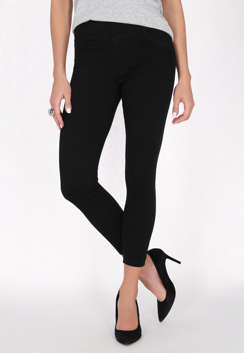 Fekete leggings sima textúrával és testhezálló fazonnal, fekete magassarkú cipővel párosítva. Az derékpánt rugalmas a kényelem érdekében.