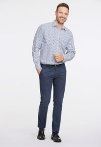 Camicetta bianca con motivo floreale blu, maniche lunghe, abbinata a chinos blu navy e scarpe stringate nere. Fit semplice e moderno.