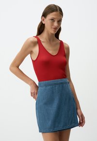Top a costine rosso con scollatura a V profonda abbinato a una mini gonna di jeans azzurri chiari con chiusura a bottoni e una texture liscia.