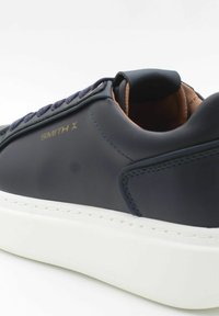 Sneaker in pelle di un blu navy scuro con una texture liscia, suola in gomma bianca e branding dorato "SMITH X" sul lato. Presenta lacci blu navy.
