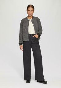 Cardigan gris texturé avec un col rond, associé à un jean noir à taille haute et large. Des chaussures à plateforme noires complètent l'ensemble.