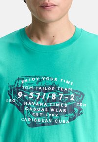 Turkis bomulds t-shirt med grafisk print af en vintage bil med hvide tekst-elementer og rund halsudskæring.