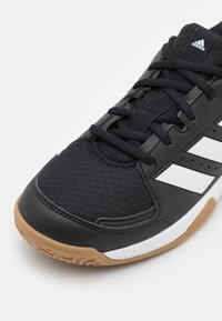 Scarpa sportiva nera con tomaia in tessuto testurizzato, design a tre strisce bianche e suola in gomma naturale. Presenta lacci neri e colletto imbottito.