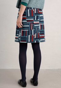 Knee-length skirt in a multicolored, geometric pattern featuring navy, red, and light blue on a textured fabric. Worn with dark tights and shoes.