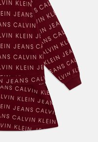 Vestido cor burdeos com um padrão repetido de "Calvin Klein Jeans" numa cor clara em contraste, com mangas compridas e um corte descontraído.