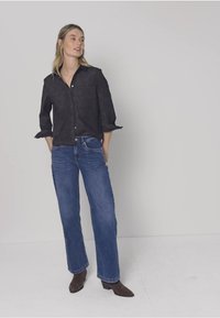 Camisa negra abotonada de tela suave, combinada con jeans de pierna ancha azul claro. El conjunto incluye puños de manga remangados y botas puntiagudas.