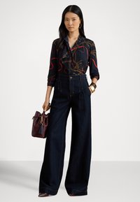 Marineblå bluse med gull- og rødt kjedemønster, høytlivs mørk denim bukser med vide ben, og en burgunderrød håndveske med duskdetalj.