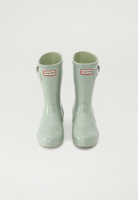 Bottes de pluie en caoutchouc vert avec une finition brillante, bout rond et détails de sangle réglable. Présente un logo de marque rouge et blanc à l'avant.