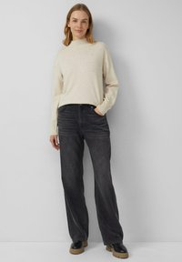 Kremowy sweter z dzianiny z wysokim kołnierzem i ozdobnymi koralikami, zestawiony z luźnymi ciemnoszarymi dżinsami i czarnymi butami na platformie.