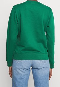 Groene sweatshirt van zacht materiaal, met een ronde hals, geribde mouwen en zoom. Gepaard met lichtblauwe jeans, die een casual pasvorm tonen.