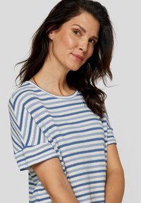 Striped knit top featuring horizontal blue and white lines, round neck, short sleeves, and textured fabric. Smooth finish with relaxed fit.