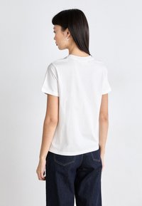 T-shirt in cotone bianco con maniche corte e scollatura rotonda, abbinato a pantaloni in denim blu scuro, visto da dietro.