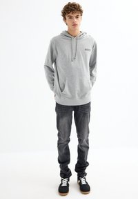 Sudadera gris con un bolsillo frontal y cordón, con la palabra "INSIDE" en negro. Combinada con jeans oscuros y zapatillas.