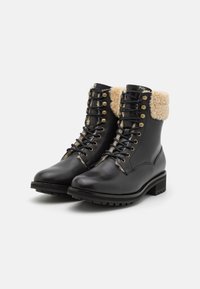 Botas negras de cuero hasta el tobillo con un borde forrado de lana, ojales dorados y cordones. Suela gruesa de goma con tracción para durabilidad y agarre.
