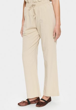 Beige, lightweight, elastic-waist trousers with a loose fit, featuring side pockets and a drawstring for adjustment. Flat front design.