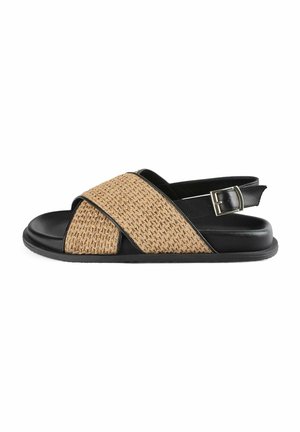 Black and tan strappy sandal featuring woven material on the strap, adjustable buckle, open toe design, and a flat rubber sole.