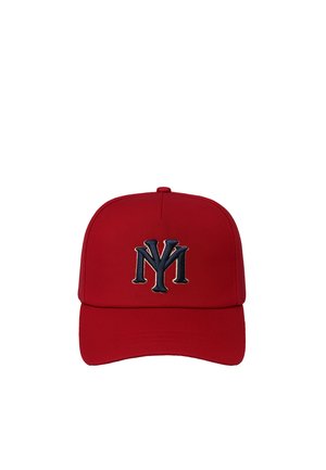 Jeune femme aux longs cheveux foncés portant une casquette rouge et un pull rayé bleu marine et blanc avec un logo rouge et bleu marine assorti sur la poitrine, fond neutre.