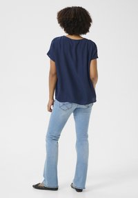 Blouse bleu marine à manches courtes avec une coupe décontractée, associée à un jean flare bleu clair et des ballerines noires, vue de dos.